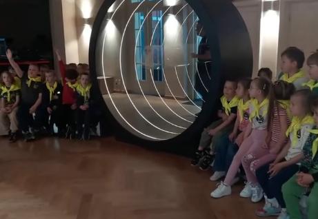Dzieci siedzą w grupie koło makiety oka.