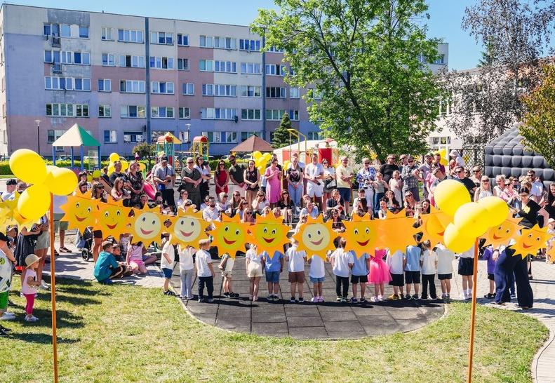 Dzieci oraz rodzice stoją w amfiteatrze , przed nimi słońca zrobione z papieru na sznurku.