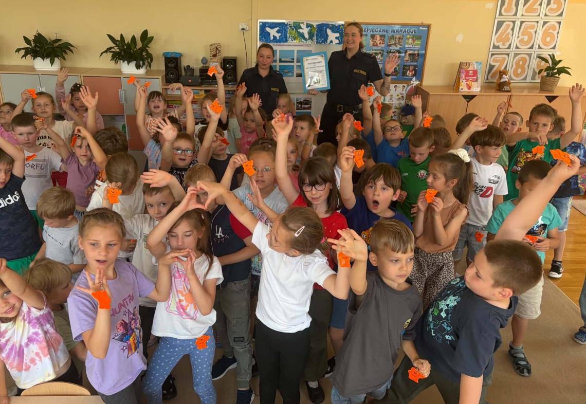 Dzieci stoją w grupie razem z paniami ze straży miejskiej w ręku trzymają odblaski.