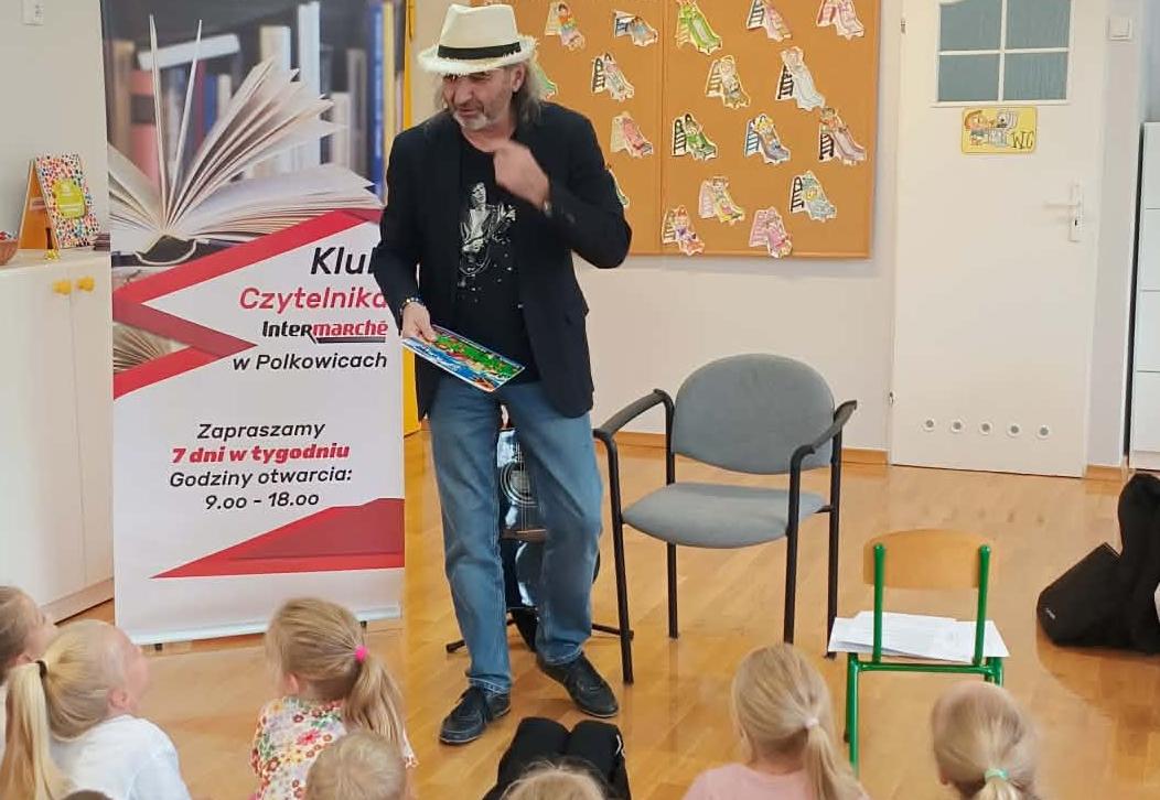 Dzieci siedząc na dywanie słuchają czytanych bajek przez autora.