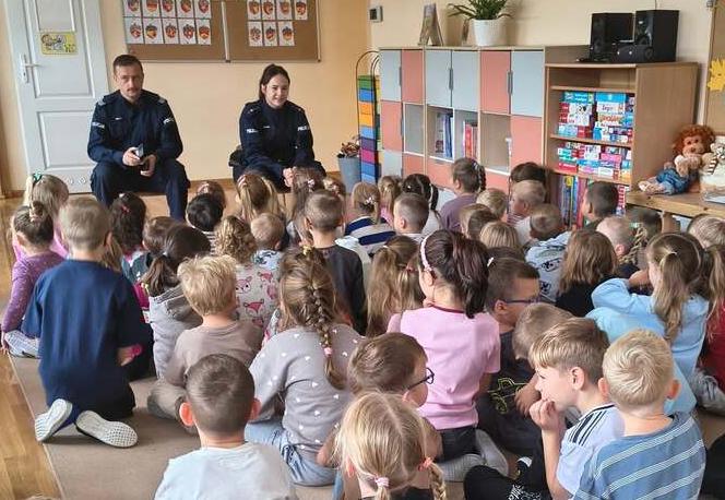 Dzieci siedzą na dywanie w grupie i słuchają policjantów.