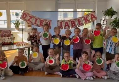 Dzieci pozują do zdjęcia na tle napisu dzień jabłka trzymając w rękach wykonane przez siebie papierowe jabłka.