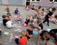 Grupa dzieci rysuje kredą na tarasie  przedszkola.